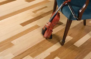 A violin resting against a chair on a light, mixed-tone hardwood floor