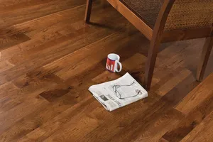 A coffee mug and a newspaper on a dark brown hardwood floor beside a chair