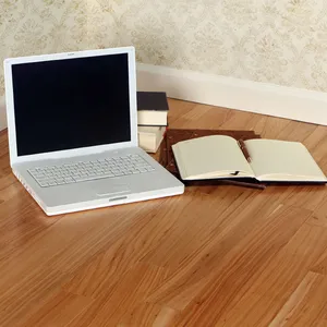 A laptop, a notebook and a pen on a light honey-colored hardwood floor